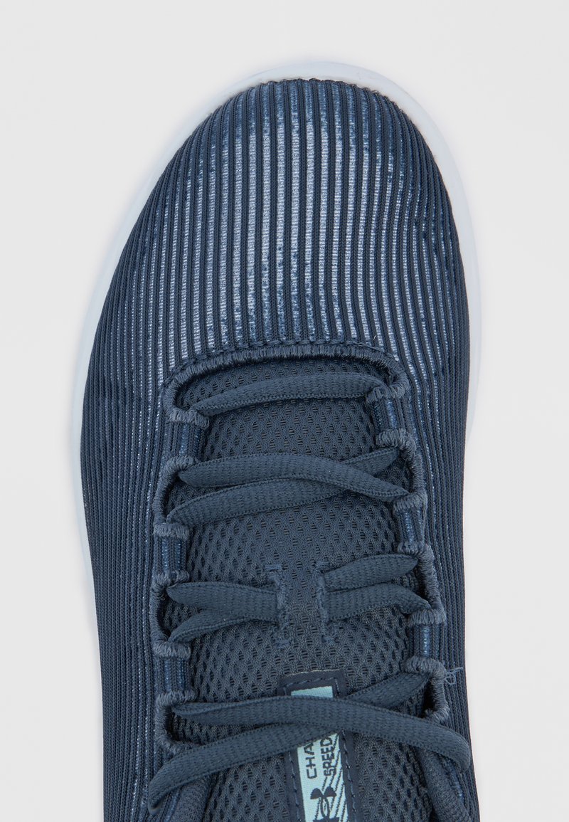 Zapatilla deportiva azul oscuro con textura acanalada y parte superior de malla, con cordones planos, cuello acolchado y suela de color claro.