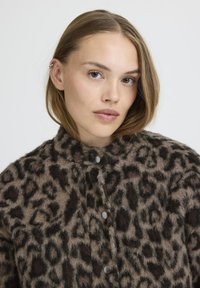 Veste en imprimé léopard, fabriquée en tissu doux et duveteux. Dotée d'un col haut et d'une fermeture à boutons à l'avant avec des boutons gris. Motif texturé dans des tons de marron.