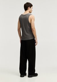 Débardeur en coton gris avec une coupe décontractée, associé à un pantalon noir ample. La tenue présente un design simple et minimaliste.