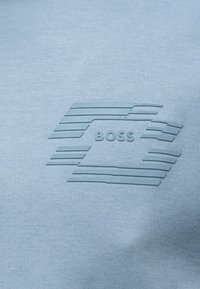 Tissu bleu clair avec logo en relief surélevé présentant des lignes horizontales et le mot "BOSS" au centre.