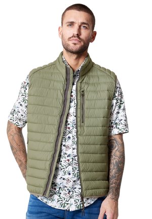 Olive green quilted vest with high collar, zip closure, and side pockets, worn over a floral short-sleeve shirt with green accents.