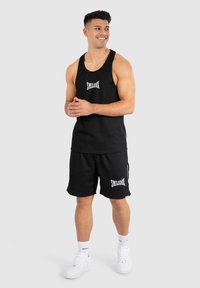 Schwarzes Tanktop und Shorts-Set mit "SMILODON"-Logo in Weiß; hat eine lockere Passform, Baumwollmaterial und weiße Sneakers für den Kontrast.