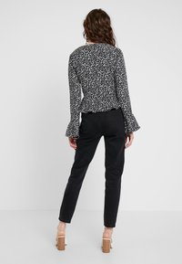 Blusa a fantasia bianca e nera con maniche a campana, abbinata a pantaloni neri aderenti e sandali con tacco. Tessuto morbido, silhouette strutturata.