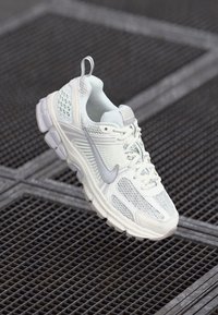 Hvite joggesko laget av mesh og syntetisk materiale, med en polstret såle, rund tå og reflekterende detaljer.