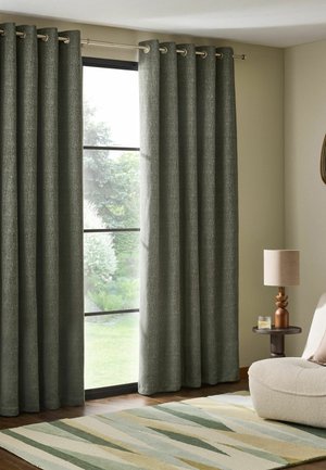 Grau strukturierte Vorhänge bedecken ein Fenster mit Gartenblick, neben einem beigen Sessel, einem hölzernen Beistelltisch, einer Lampe und einem gestreiften Teppich.