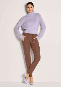 Lila gebreide turtleneck trui, bruine broek met koord en zakken, en lichtpaarse hoge hakken, gepresenteerd tegen een neutrale achtergrond.