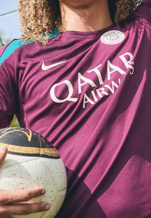 Person trägt ein lila Paris Saint-Germain Fußballtrikot und hält einen weißen und schwarzen Nike Fußball nahe an der Brust.