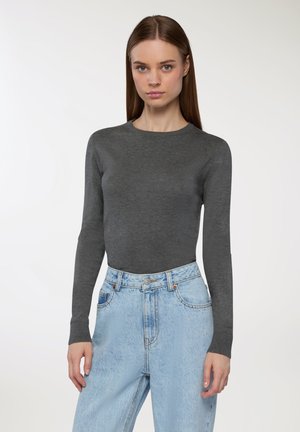Maglione aderente grigio a maniche lunghe con scollo rotondo, abbinato a jeans azzurri a vita alta, che mostrano una texture liscia e un design minimal.