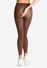 Leggings marroni con una texture liscia e una vita alta, caratterizzati da un design aderente e abbinati a scarpe bianche chunky.