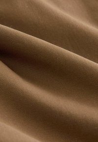 Bruine stof met een gladde textuur, voorzien van diagonale ribbels. Het oppervlak lijkt licht glanzend, met zachte plooien en kreukels.