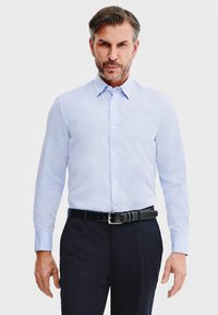 Jasnoniebieska koszula z długim rękawem i kołnierzykiem zapinanym na guziki, w połączeniu z ciemnymi spodniami i czarnym skórzanym paskiem; gładka tekstura, dopasowany krój.