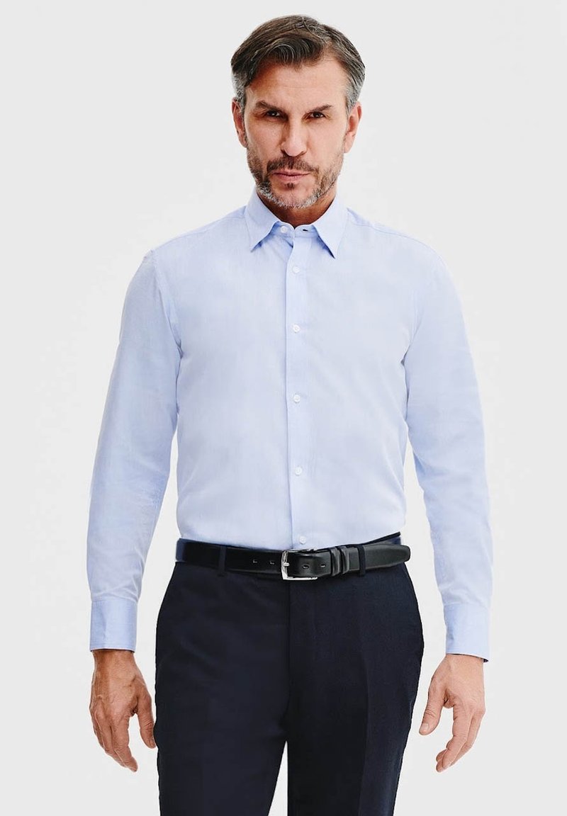 Jasnoniebieska koszula z długim rękawem i kołnierzykiem zapinanym na guziki, w połączeniu z ciemnymi spodniami i czarnym skórzanym paskiem; gładka tekstura, dopasowany krój.