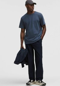 T-shirt bleu marine, tissu doux, col rond, associé à un pantalon sombre assorti. Une veste sombre et des baskets avec des accents blancs et noirs.