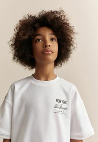 Hvid bomulds t-shirt med korte ærmer, rund halsudskæring, med trykte tekster "NEW YORK" og "Five Boroughs" i sort. Glat tekstur.