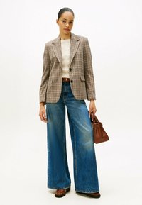 Blazer à carreaux aux tons gris et marron, associé à un jean denim bleu à jambes larges. Comprend un pull léger et un petit sac à main marron.