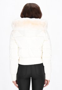 Hvid dunjakke med hætte foret med faux pels. Har en figursyet silhuet, ribbede manchetter og kant. Glat, skinnende materiale med quiltet design.