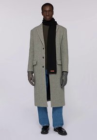 Šedý vlněný kabát s klopami s výřezem, černý šátek, žebrovaná textura, v kombinaci s modrými džínami a koženými botami, doplněný šedými rukavicemi.