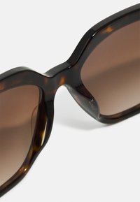 Schildpatt-Sonnenbrille mit dunklen Verlaufslinsen, übergroßer quadratischer Form und glänzender Oberfläche. Mit dezenten Akzenten an den Bügeln verziert.