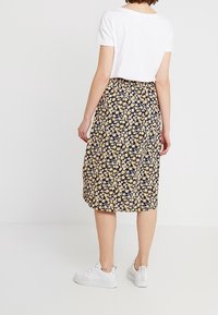 Jupe fleurie sur fond marine avec des fleurs jaunes et blanches, longueur genoux, en tissu léger. Associée à un haut blanc à manches courtes et des baskets blanches.