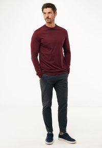 Bordowa koszula z długim rękawem i ciemnoszare spodnie na męskim modelu, charakteryzujące się prostym wzornictwem i dopasowanym krojem. Granatowe trampki dopełniają stylizację.