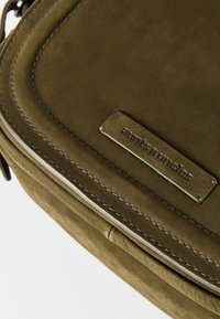 Grüne Wildledertasche mit abgerundeten Kanten, silberner Hardware und einem Metallschild "aunts & uncles". Texturierte Oberfläche mit sichtbaren Nähdetails.