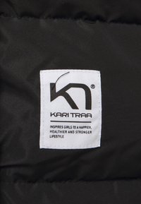Schwarzer Daunenstoff mit einem weißen Etikett, das das Logo "K" und den Text trägt: "KARI TRAA BEGEISTERT MÄDCHEN FÜR EIN GLÜCKLICHERES, GESÜNDERES UND STÄRKERES LEBENSSTIL."