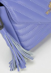Fioletowa skórzana torebka z ukośnym pikowaniem, srebrnymi przeszyciami oraz dekoracyjnym frędzlem w jasnoniebieskich i srebrnych akcentach.