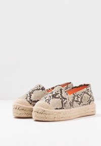 Espadrillas con una suola in juta intrecciata di tonalità marrone e abbronzata e una tomaia in tessuto beige e marrone a motivo di pelle di serpente. Punta leggermente arrotondata e lati elastici.