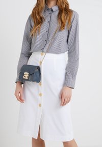 Skjorta med knappar i tunna blå och vita ränder, kombinerad med en vit kjol med guldknappar och en blå axelremsväska med gulddetaljer.