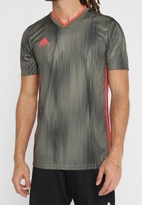 Kortärmad grå träningsskjorta med svart prickigt mönster, rosa detaljer och v-ringad design. Tillverkad av lätt, andningsbart material.