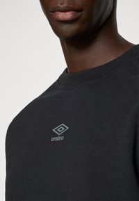 Čierne bavlnené tričko s ribbed okrúhlym výstrihom, s malým šedým logom Umbro na hrudi. Hladká textúra a voľný strih.