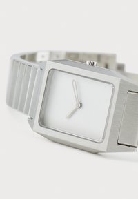 Reloj de acero inoxidable plateado con una esfera rectangular, dial blanco, manecillas mínimas de horas y minutos, y una correa de metal cepillado.