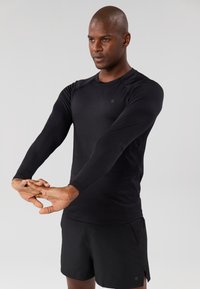 Long-sleeve black athletic shirt made of smooth fabric; features a round neckline and fitted design, paired with black shorts.