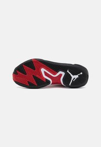 Semelle de basket noire et rouge avec motif en zigzag et logo Jumpman blanc sur le talon sur fond blanc.