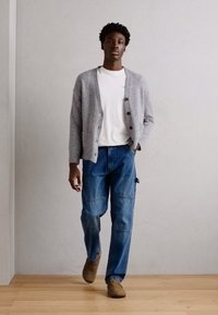 Grå strikket cardigan over en hvit T-skjorte, kombinert med blå denim cargo-bukser. Modellen har på seg brune slip-on sko. Enkel design, avslappet passform.