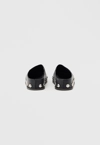 Black flat shoes with a low profile, featuring silver studs along the side and a smooth leather texture. Open back design.