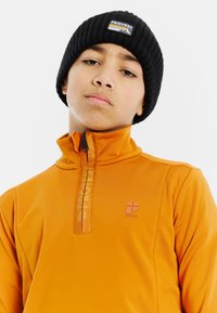 Pomarańczowy polar z suwakowym zapięciem w ćwiartce, w zestawie z czarną dzianinową czapką; posiada zamek z przodu i subtelne logo na klatce piersiowej.