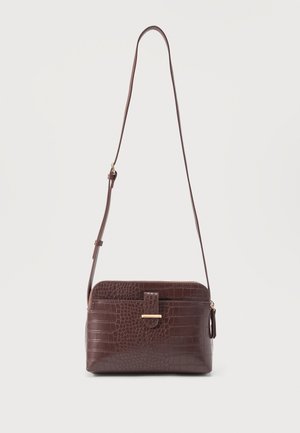Sac bandoulière en cuir embossé façon croco marron avec sangle réglable et poche avant à rabat sur fond uni.