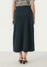 Donker teal maxi rok met een gladde textuur, een elastische tailleband en een subtiele flare, gecombineerd met zwarte blokhakken sandalen.