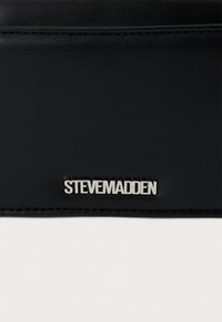 Fekete, szintetikus pénztárca dombornyomott ezüst "STEVE MADDEN" logóval. Sima textúra, finom varrási részletekkel a széleken.