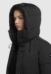 Schwarze gepolsterte Jacke mit großer Kapuze,Frontreißverschluss und Druckknöpfen. Verfügt über verstellbare Kordelzüge und ein Logopatch am Ärmel.