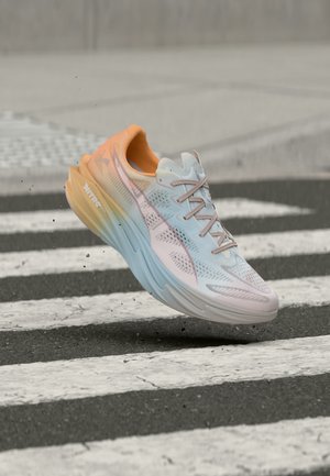 Lekki but do biegania z pastelową gradientową podeszwą, białą siateczkową cholewką i sznurowadłami, unoszący się nad czarno-białym przejściem dla pieszych.