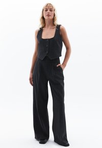 Schwarze Nadelstreifenweste und weite Hose, die Knöpfe, ein kurzes Design und eine weiche Stofftextur aufweisen. Das Outfit hat eine taillierte Optik.