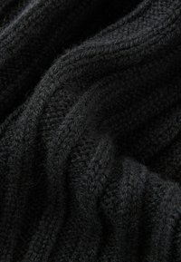 Schwarzer Strickstoff mit einem strukturierten Muster, das Rillen und weiche Fasern aufweist. Zeigt ein welliges und fallendes Aussehen.
