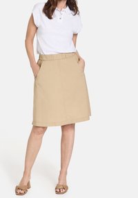 Khaki A-linjainen hame, jossa on joustava vyötärö, sivutaskut ja sileä puuvillakangas. Yhdistetty valkoisen kauluspuseron kanssa.