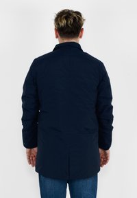 Cappotto blu navy con maniche lunghe, taglio dritto e spacco posteriore. Realizzato in tessuto liscio senza motivi visibili o dettagli in metallo.