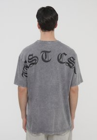 T-shirt grigio oversize con lavaggio sbiadito. Presenta una scritta audace nera sul retro in un font stilizzato. Maniche corte e collo rotondo.