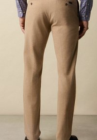 Helle Wollhose mit Gesäßtaschen, geraden Beinen und subtiler Textur. Das Hemd des Trägers hat ein blau-rotes Karomuster.