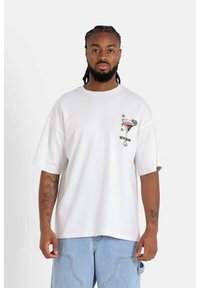 Vit oversized t-shirt i bomull, med en grafisk design av ett cocktailglas och text på vänster bröst i svart och röd.