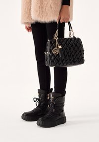 Schwarze geflochtene Lederhandtasche mit goldfarbenen Beschlägen und Quasten-Detail, kombiniert mit schwarzen gepolsterten Knöchelstiefeln mit dicken Sohlen und Schnürsenkeln.